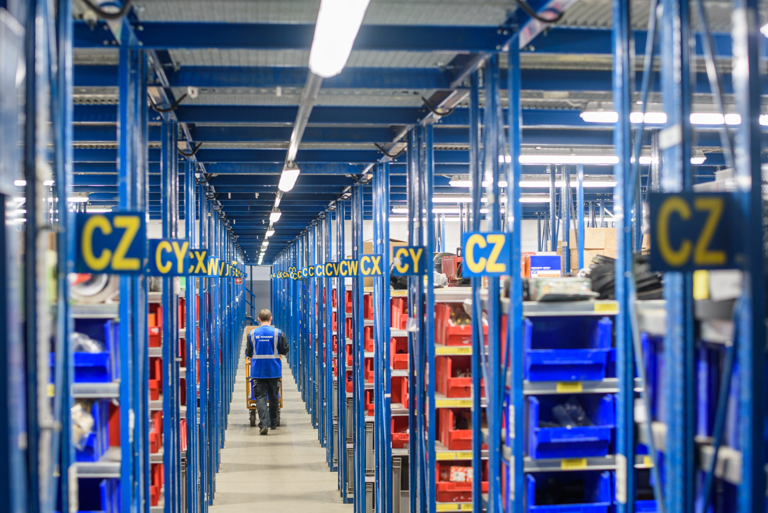 Pracownik Kramp Logistics w oświetlonym magazynie z systemem regałowym