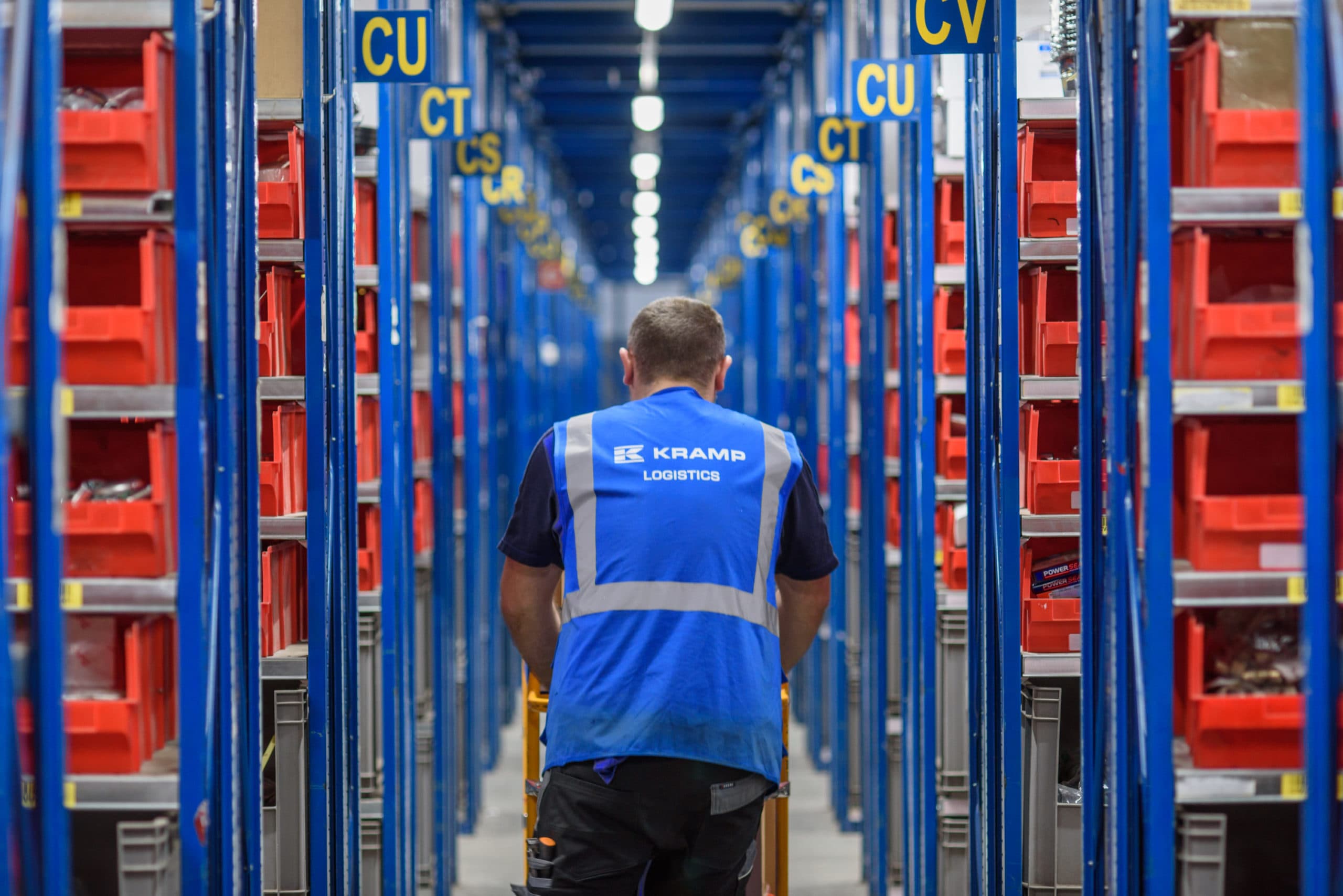 Pracownik Kramp Logistics w oświetlonym magazynie z systemem regałowym