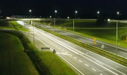 Nocne oświetlenie LED na węźle autostradowym z wysokimi masztami oświetleniowymi i widocznym ruchem pojazdów
